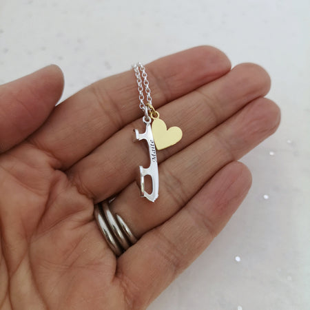 hand holding a silver necklaces which has a personalised silver ice skate blade charm and a gold heart charm