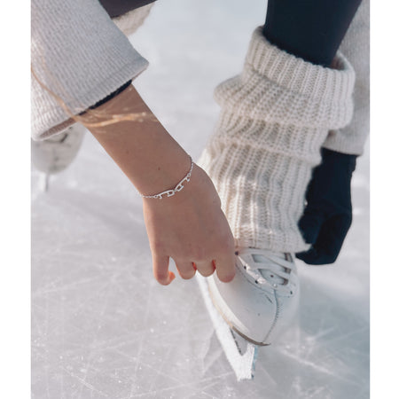 hand with a silver bracelet with two tiny interlinked silver ice skating blades