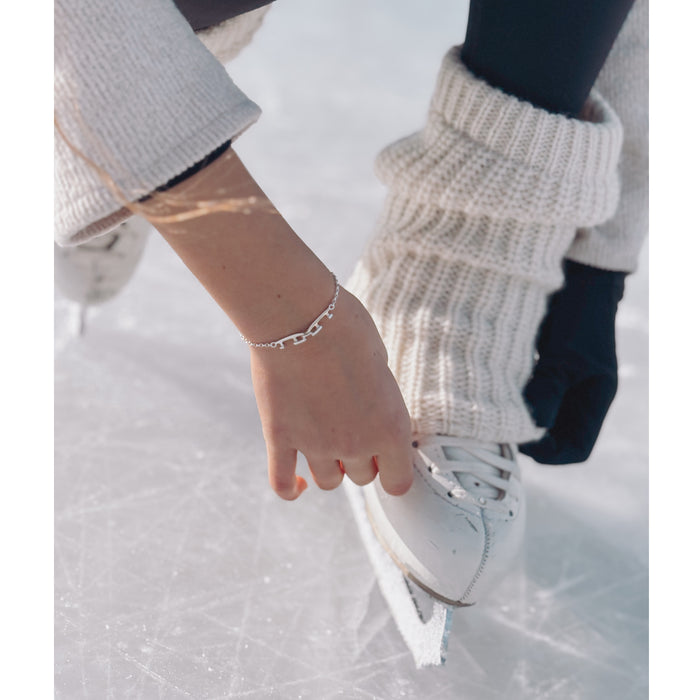 hand with a silver bracelet with two tiny interlinked silver ice skating blades