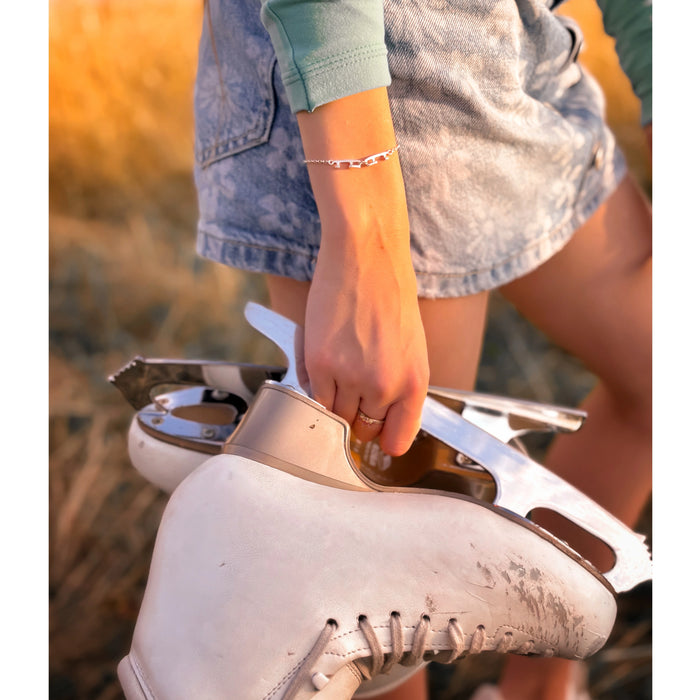 Close-up of a person holding a white ice skate wearing a silver ice skating blade bracelet with a blurred natural background