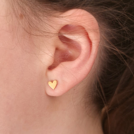 close-up image of a girl wearing a gold plated heart stud earring