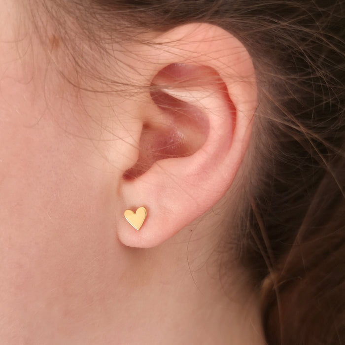 close-up image of a girl wearing a gold plated heart stud earring