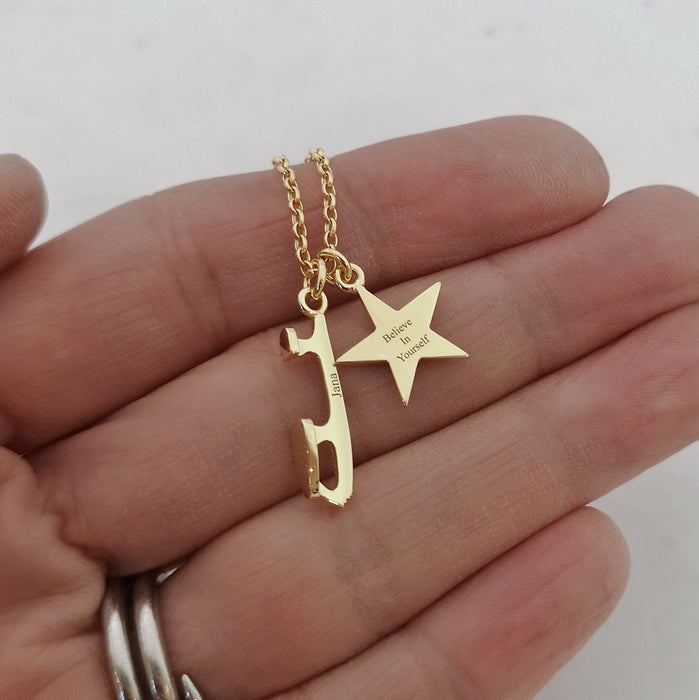 close up of a gold necklace with a skate blade and a heart charm, both are engraved