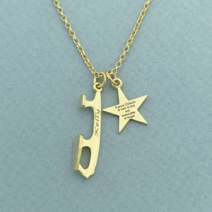 a gold necklace with an ice skate blade and heart charm on a blue background, the charms are engraved