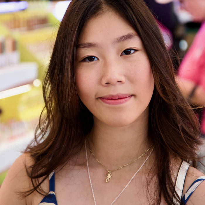 Young woman with long brown hair and a gold necklace in a blurred indoor setting
