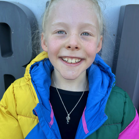 Child wearing a colorful jacket wearing a silver necklace with a snowflake and ice skate blade charm with a blurred background