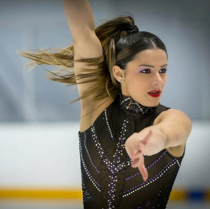 figure skater performing on ice in a sparkly black dress wearing a personalised gold ice skate blade necklace