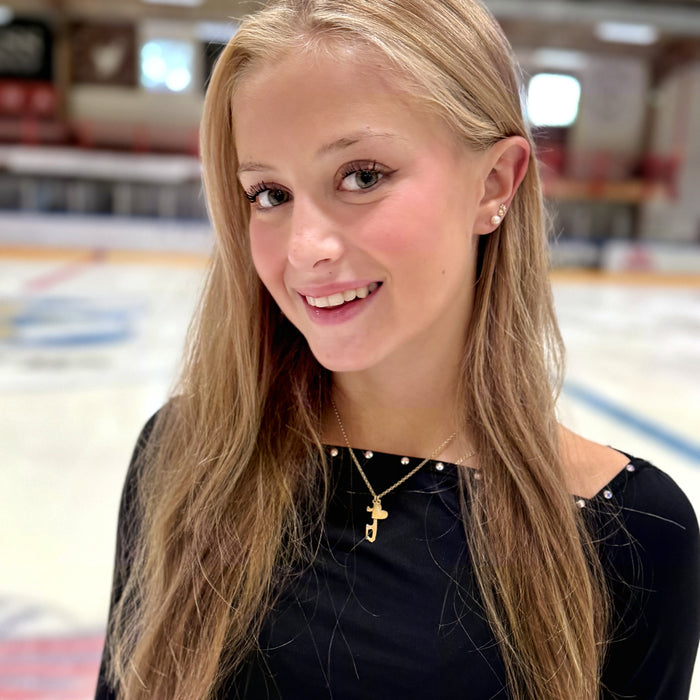 close up image of female figure skater on ice wearing a black top and a gold ice skate blade necklace