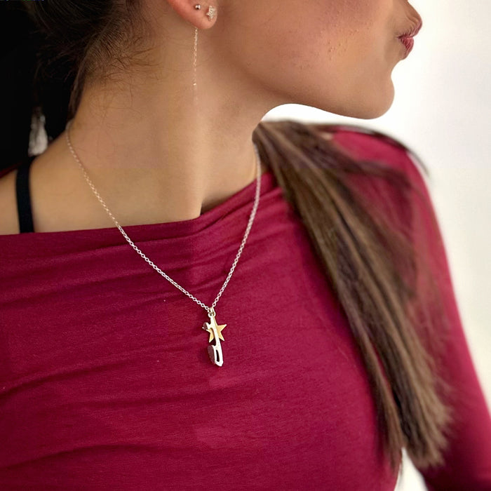 close up of an ice skater in a dark red top next to an ice rink wearing and ice skating necklace featuring a silver skate blade and a gold star