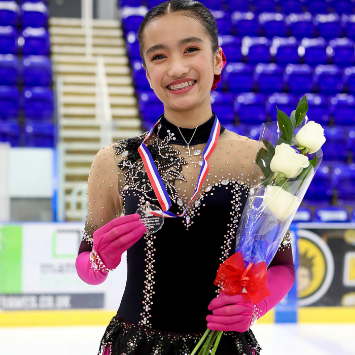 a female figure skater in a sparkly black dress holding a medal and flowers