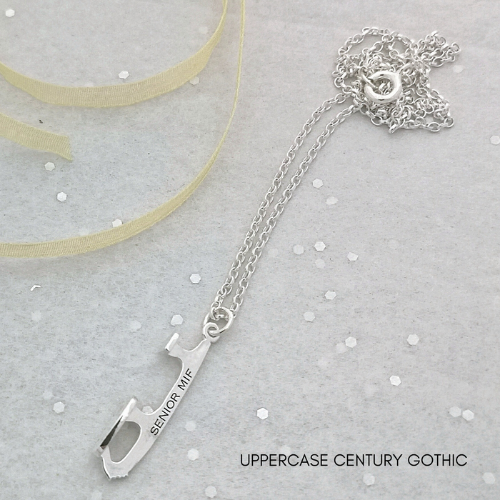 close up of an ice skate blade necklace with engraving on a grey background