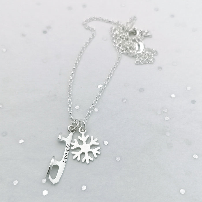 close up image of a silver ice skate blade and snowflake charm necklace  engraved with the name laura and a heart