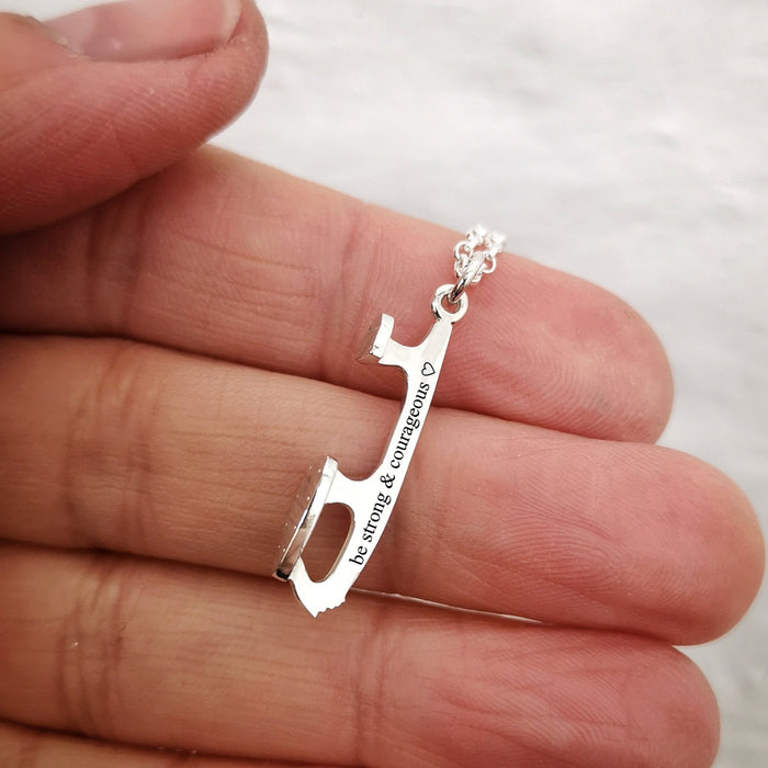 close up of a personalised silver ice skate blade necklace, the engraving reads 'be strong and courageous'