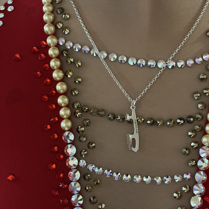 close up of a sparkly ice skating dress and an engraved ice skate blade necklace