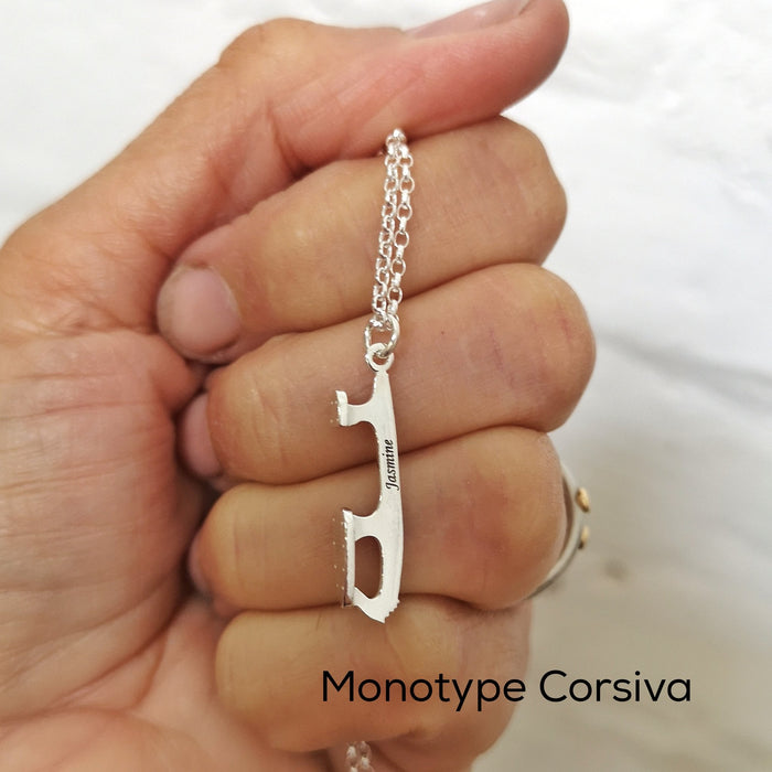 close up of a hand holding a silver ice skate blade necklace which has a name engraved on it