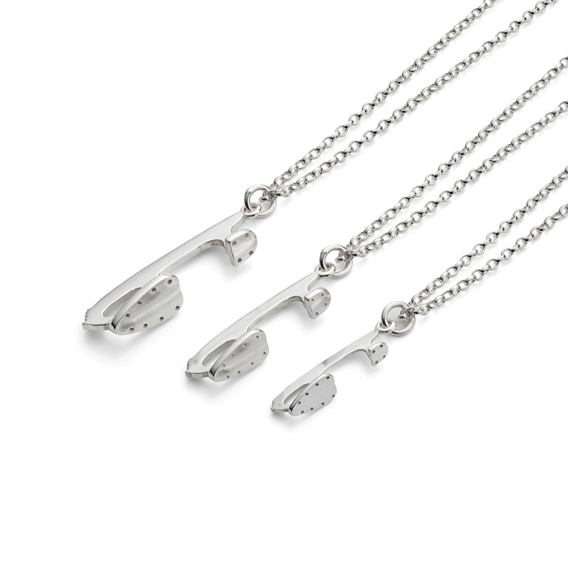 three silver ice skate blade necklaces on a white background