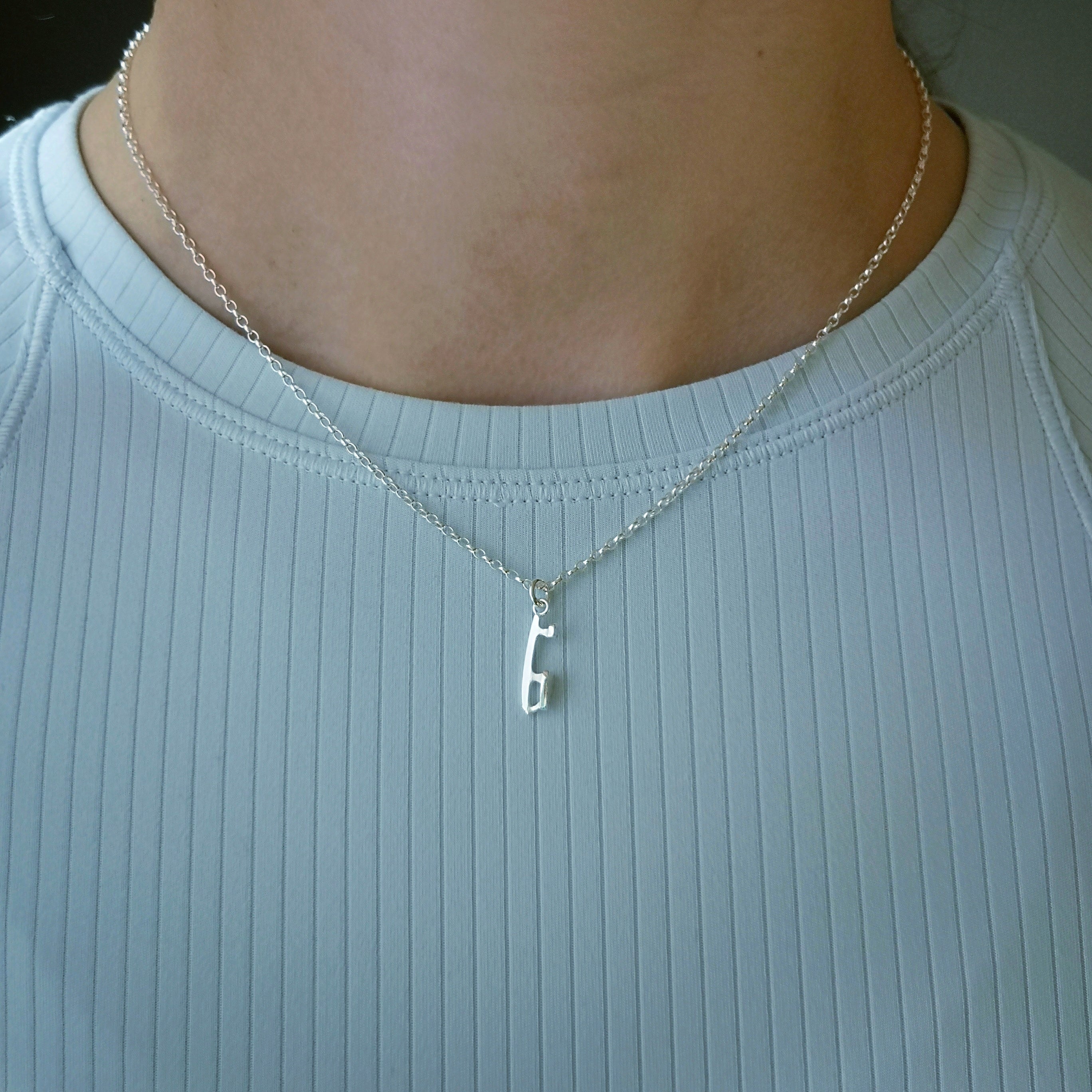 close up of a female figure skater in a blue top wearing a mini silver ice skating necklace