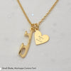 Gold necklace with a heart and an ice skate blade charm, both charms are engraved on a pale grey background