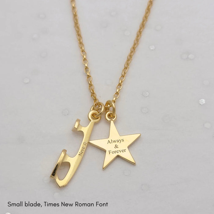 Gold necklace with a star charm and an ice skate blade charm, both charms are engraved on a pale grey background