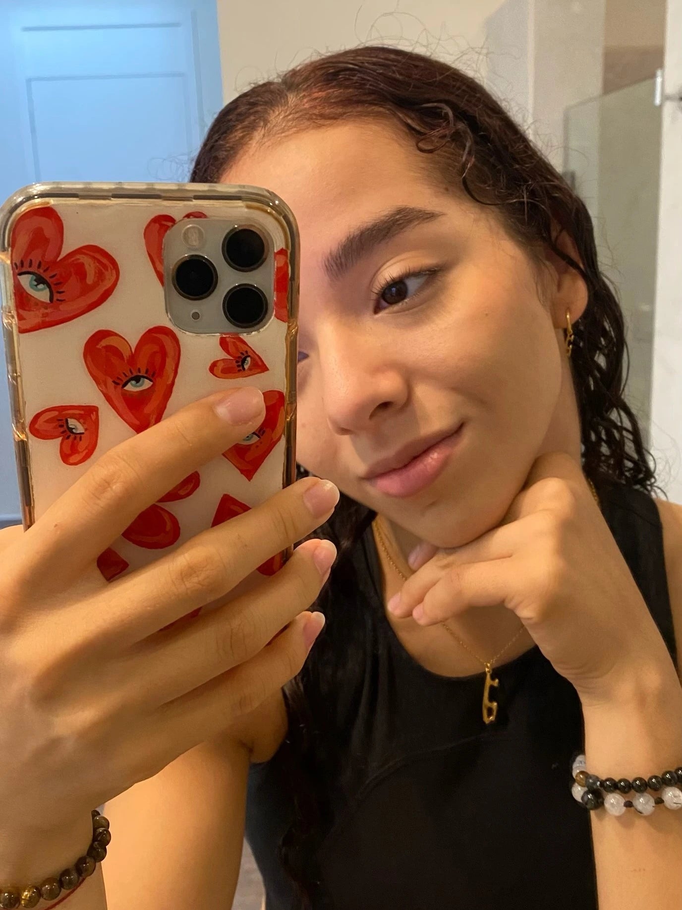 figure skater taking a selfie with her phone wearing a black top and a personalised gold ice skating necklace
