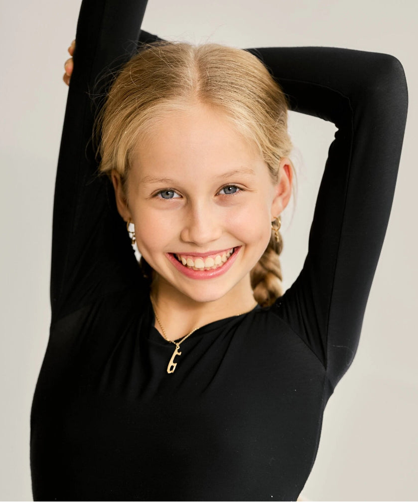 skater in a black top wearing a gold ice skate blade necklace and earrings