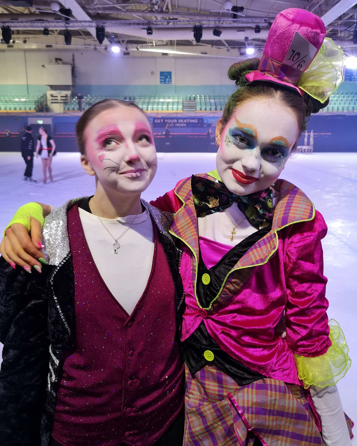 two figure skaters dressed as the white rabbit and the mad hatter standing on ice wearing ice skating jewellery necklaces