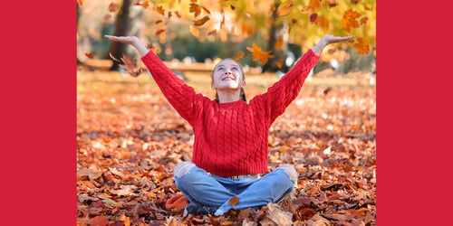 girl in a red jumper sitting cross legged amongst autumn leaves