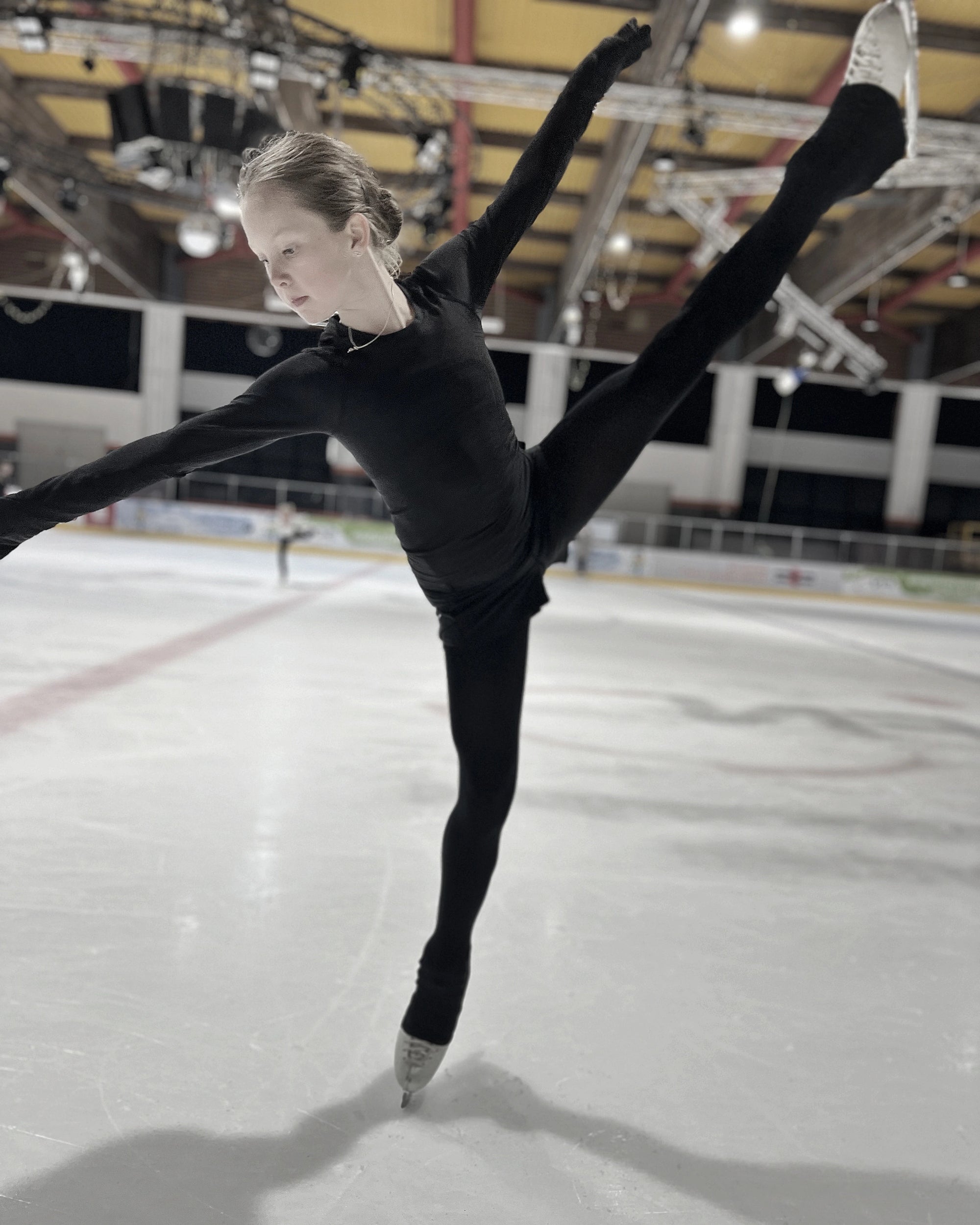 Young figure skater practising stretching positions on ice during training