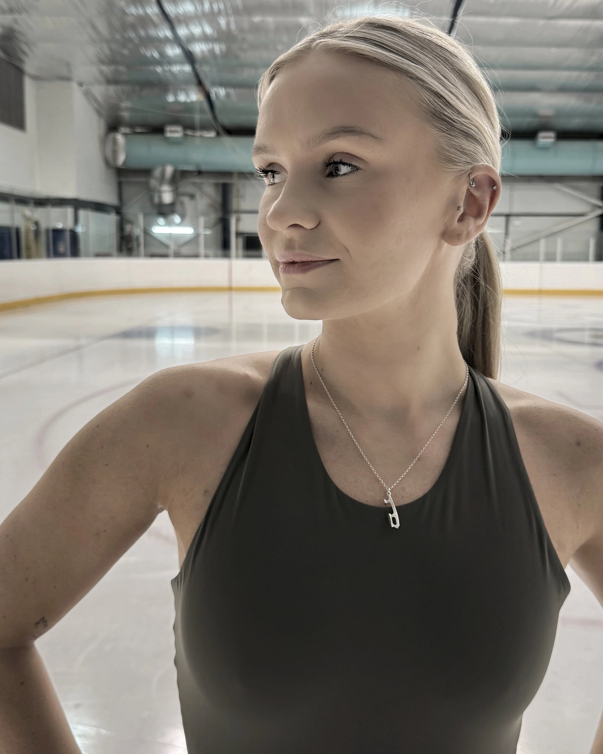 a figure skater standing on ice wearing a silver ice skate blade necklace and a green top