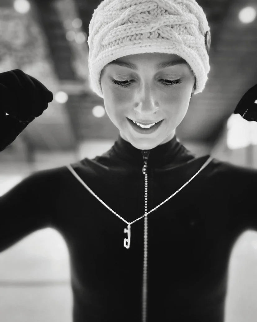 figure skater wearing a headband and gloves holding a silver ice skating blade necklace and smiling