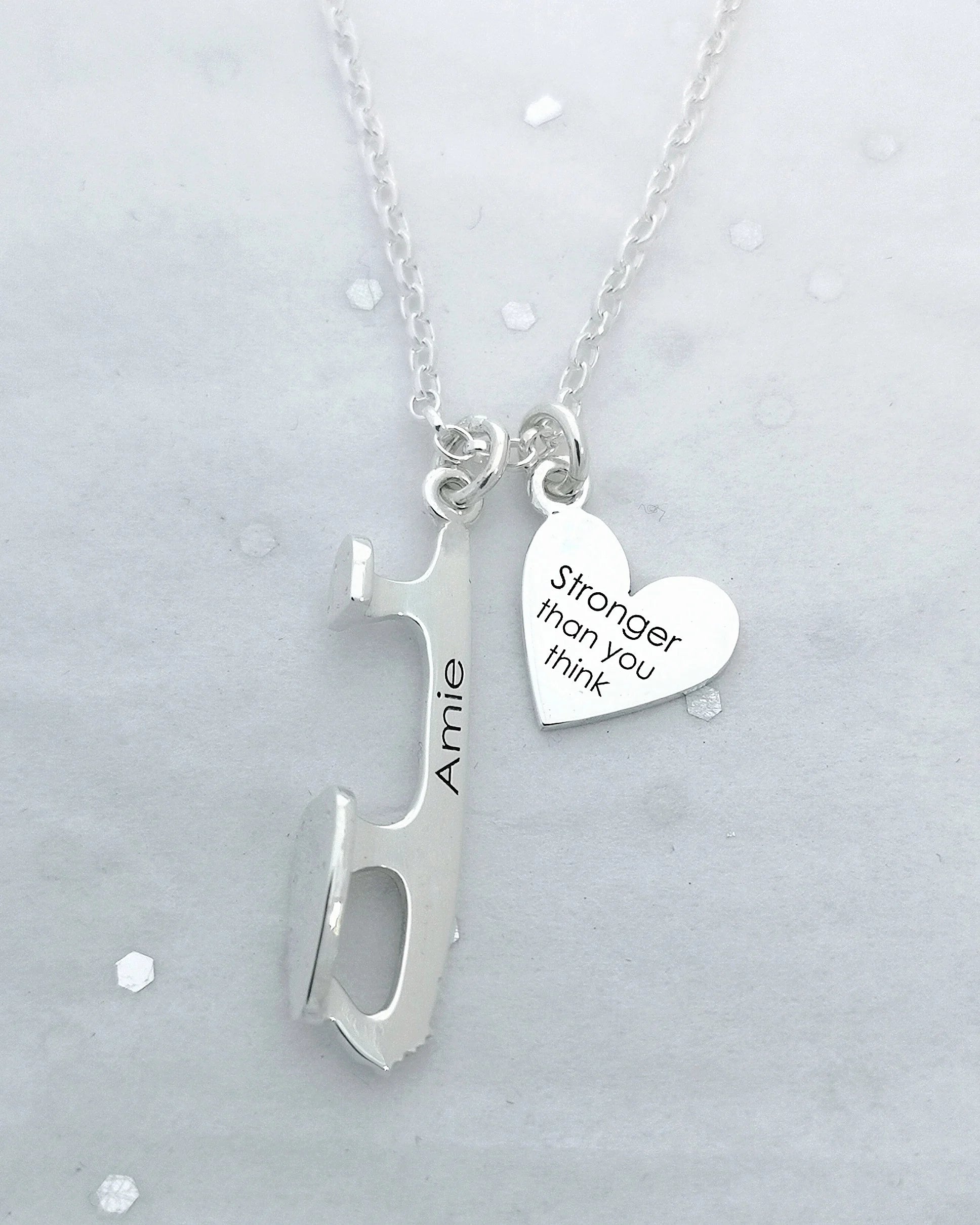 an image of a necklace with a silver ice skate blade and a heart the blade is engraved with amie and the heart engraving says 'stronger than you think'