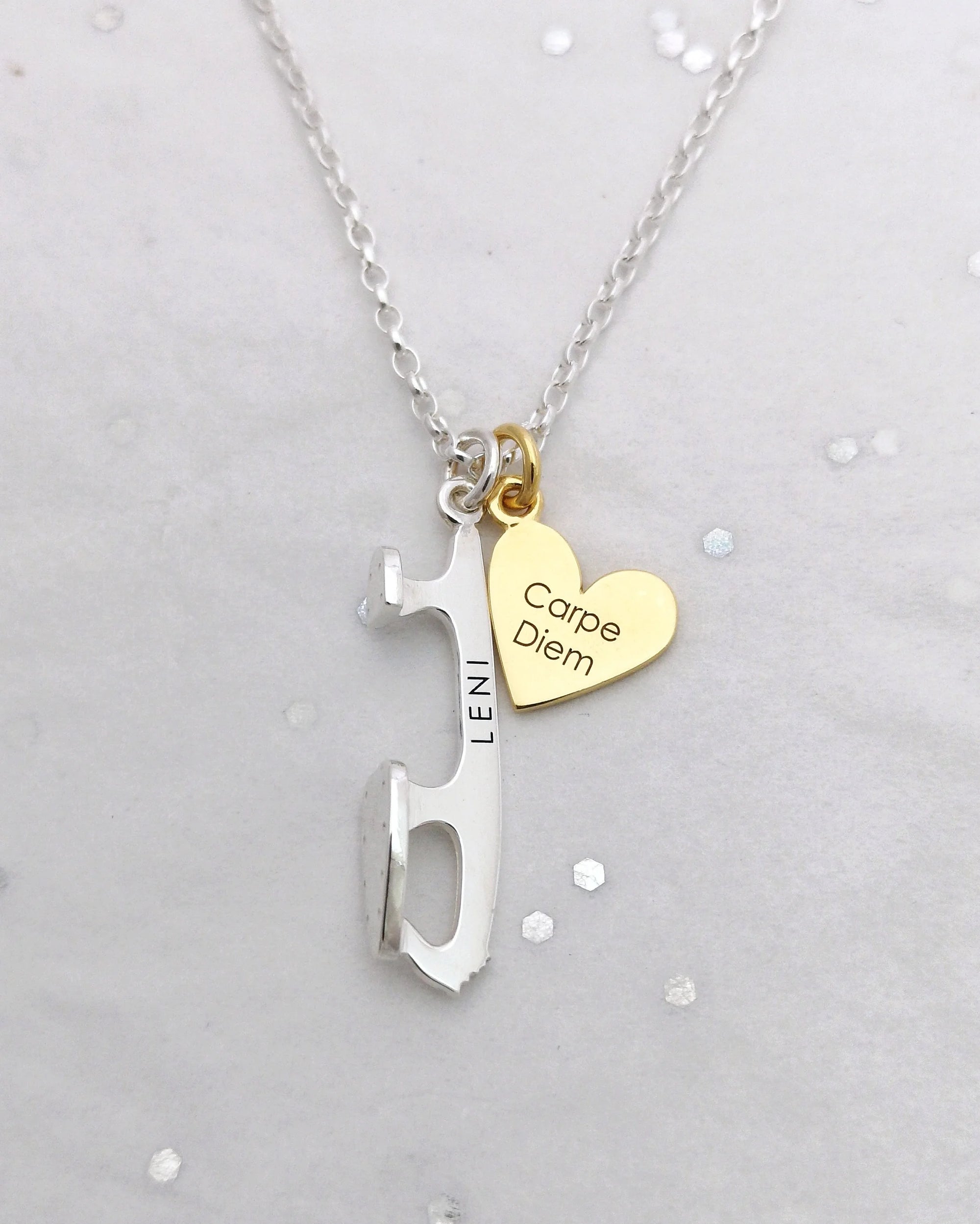 Close-up of silver and gold necklace with engraved ice skate blade charm ‘LENI’ and gold heart charm ‘Carpe Diem’