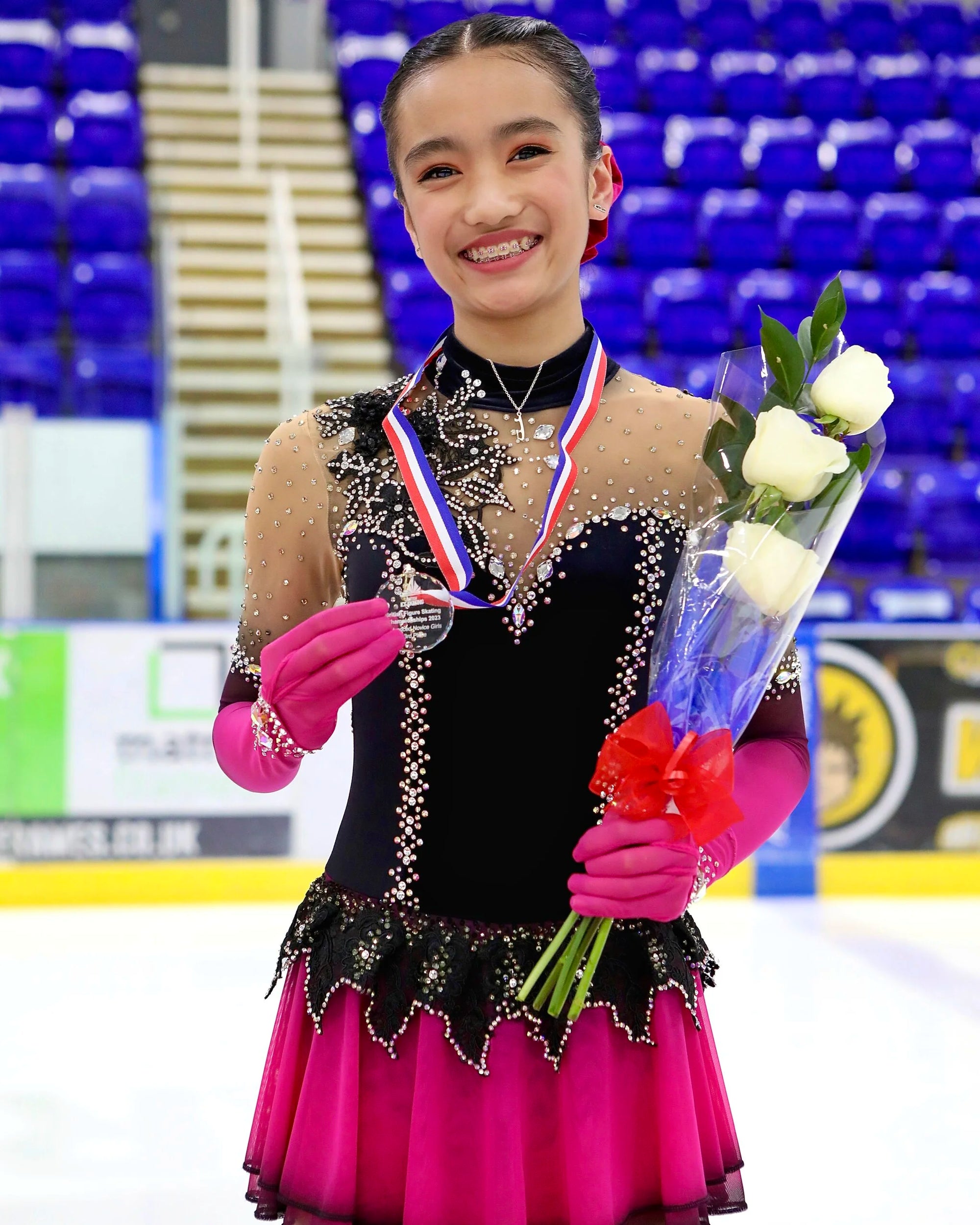 skater in a sparkly costume standing on apodium on ice holding her winning medal and a bunch of flowers