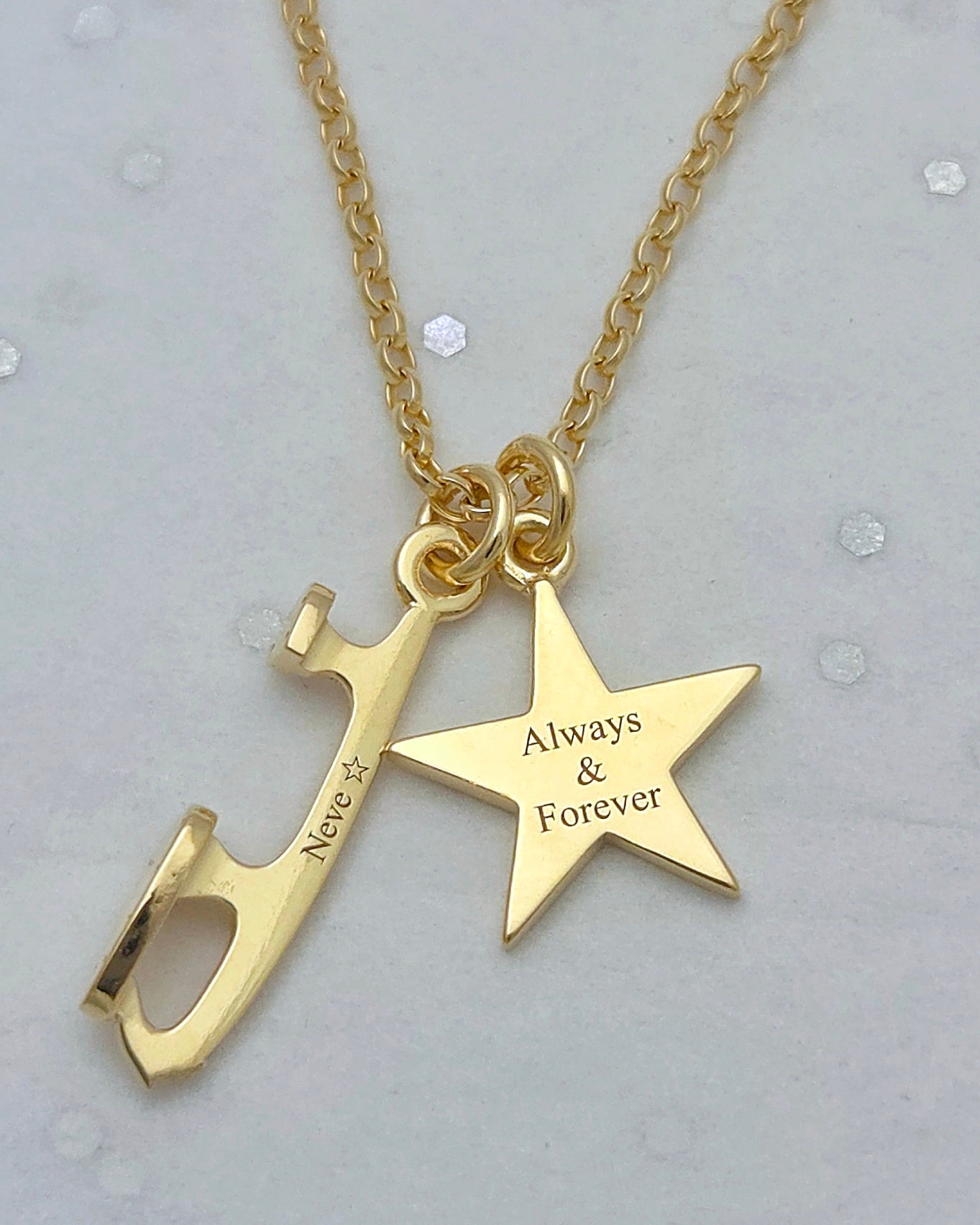 close-up of a gold ice skating necklace with 'Neve' engraved along on the tiny ice skating blade charm and 'Always & Forever' engraved on the star charm