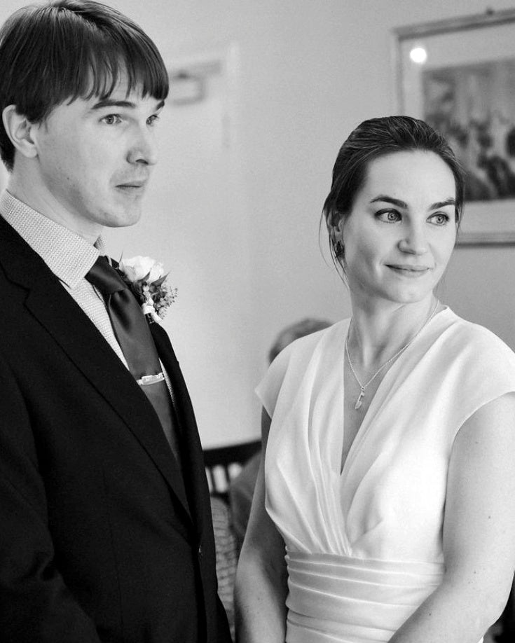Bride and groom standing together before their wedding, bride wearing silver ice skating necklace and groom wearing ice skate blade tie clip, looking nervous and excited.