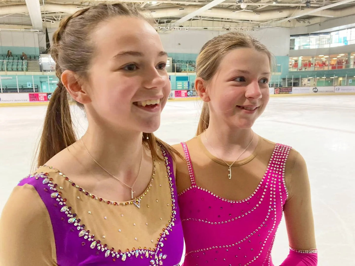 two figure skaters on ice in sparkly pink and purple dresses wearing silver ice skating necklaces