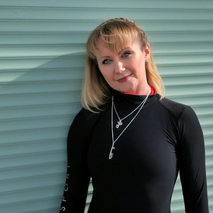 Woman wearing a black long-sleeve top with a red collar against a green metal shutter.