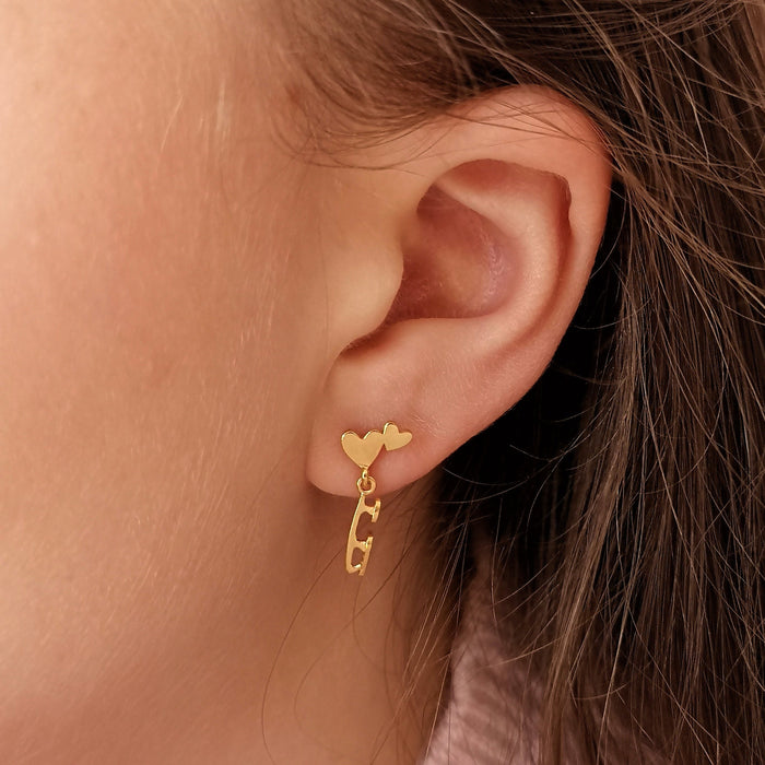 ice skater wearing gold stud earrings featuring hearts and a dangling skate blade