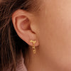 skater wearing gold stud earrings featuring hearts and a dangling skate blade