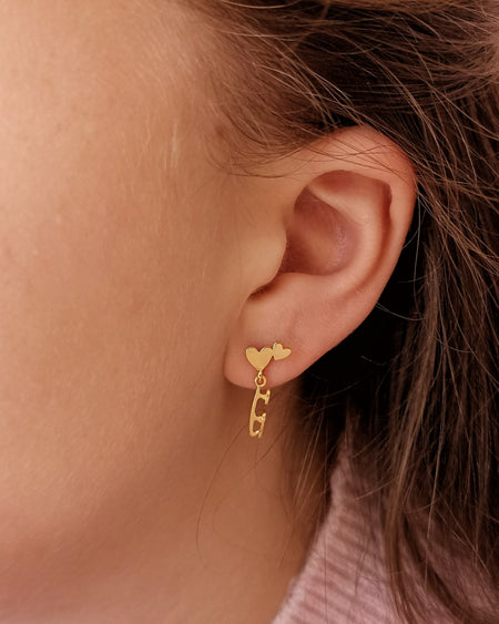 skater wearing gold stud earrings featuring hearts and a dangling skate blade