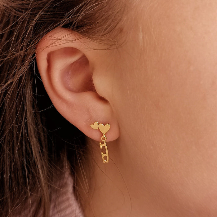 skater wearing gold stud earrings featuring hearts and a dangling skate blade