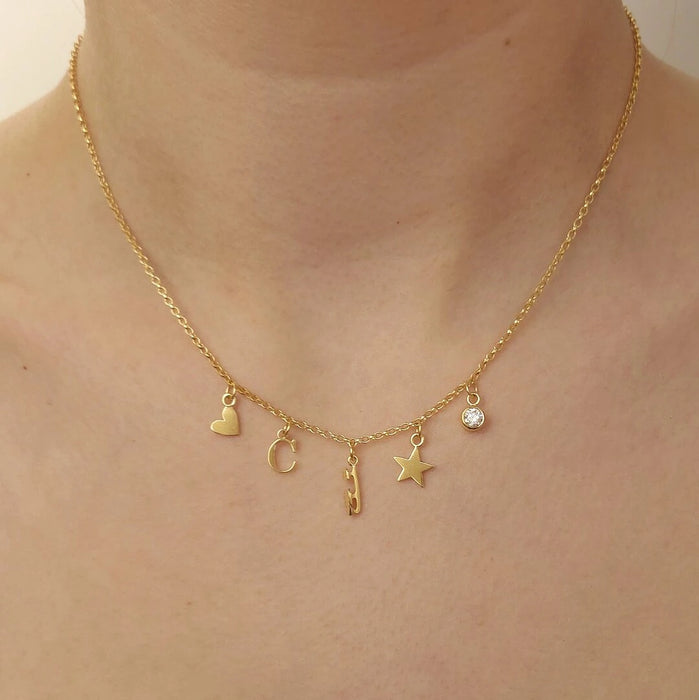 Close up of a gold necklace with five tiny charms on a person 