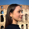 figure skater standing in front of the coliseum in Rome wearing gold shine bright ice skating stud earrings