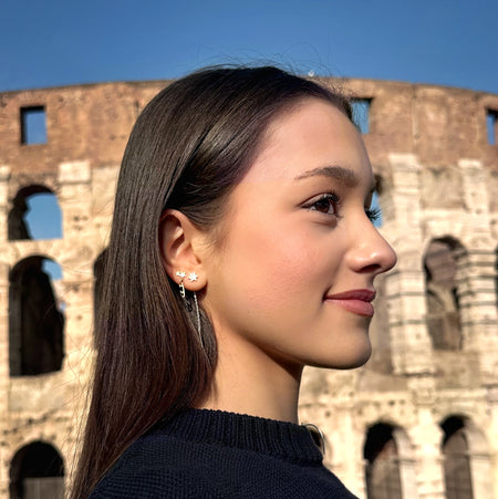 figure skater standing in front of the coliseum in Rome wearing gold shine bright ice skating stud earrings