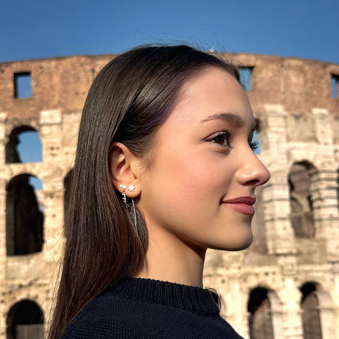 figure skater standing in front of the coliseum in Rome wearing gold shine bright ice skating stud earrings