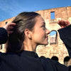 figure skater standing in front of the coliseum in Rome wearing gold shine bright ice skating stud earrings