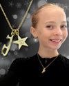 Young girl wearing a gold necklace with a star pendant and 'Believe in Yourself' message, against a blurred background.
