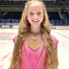 Figure skater standing on ice in a pink sparkly competition dress, she is wearing a gold ice skating necklace