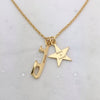 Gold necklace with a   star charmand an ice skate blade charm, both charms are engraved, on a pale grey background