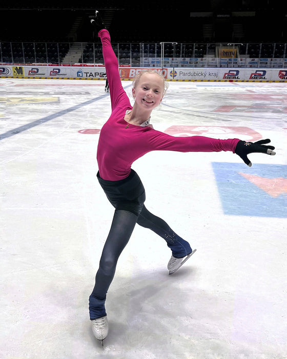 Person in a pink top and black pants skating on an ice rink.